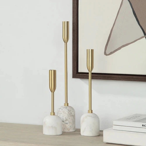 Three gold-tone taper candlesticks with cylindrical marble bases in white and light gray, arranged in ascending height on a plain white background.