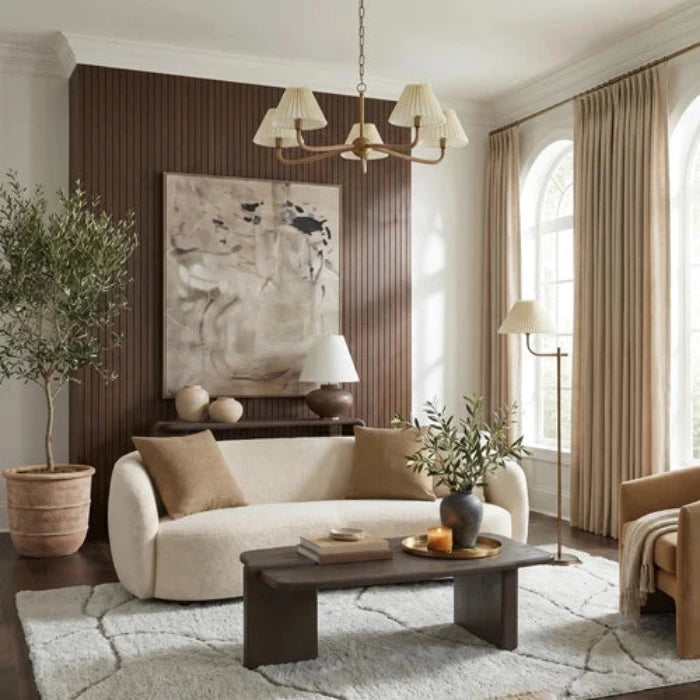 A five-light chandelier with a warm brass-finished metal frame, pleated off-white fabric shades, and a hanging chain, shown against a plain white background.