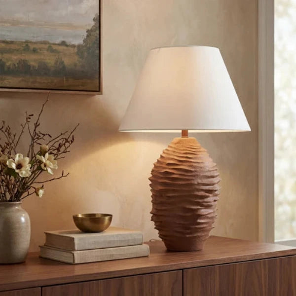 A table lamp with a textured, ribbed ceramic base in a warm brown tone and a white tapered fabric shade, shown lit against a plain white background.