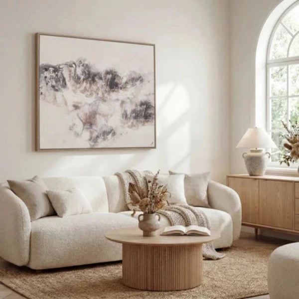 An abstract framed painting featuring textured brushstrokes in shades of gray, brown, and black over a warm off-white background, enclosed in a thin light wood frame.