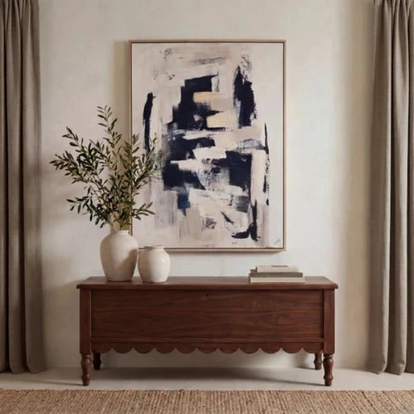 An abstract framed painting featuring layered brushstrokes in black, navy, beige, and white on a light background, enclosed in a thin metallic frame.